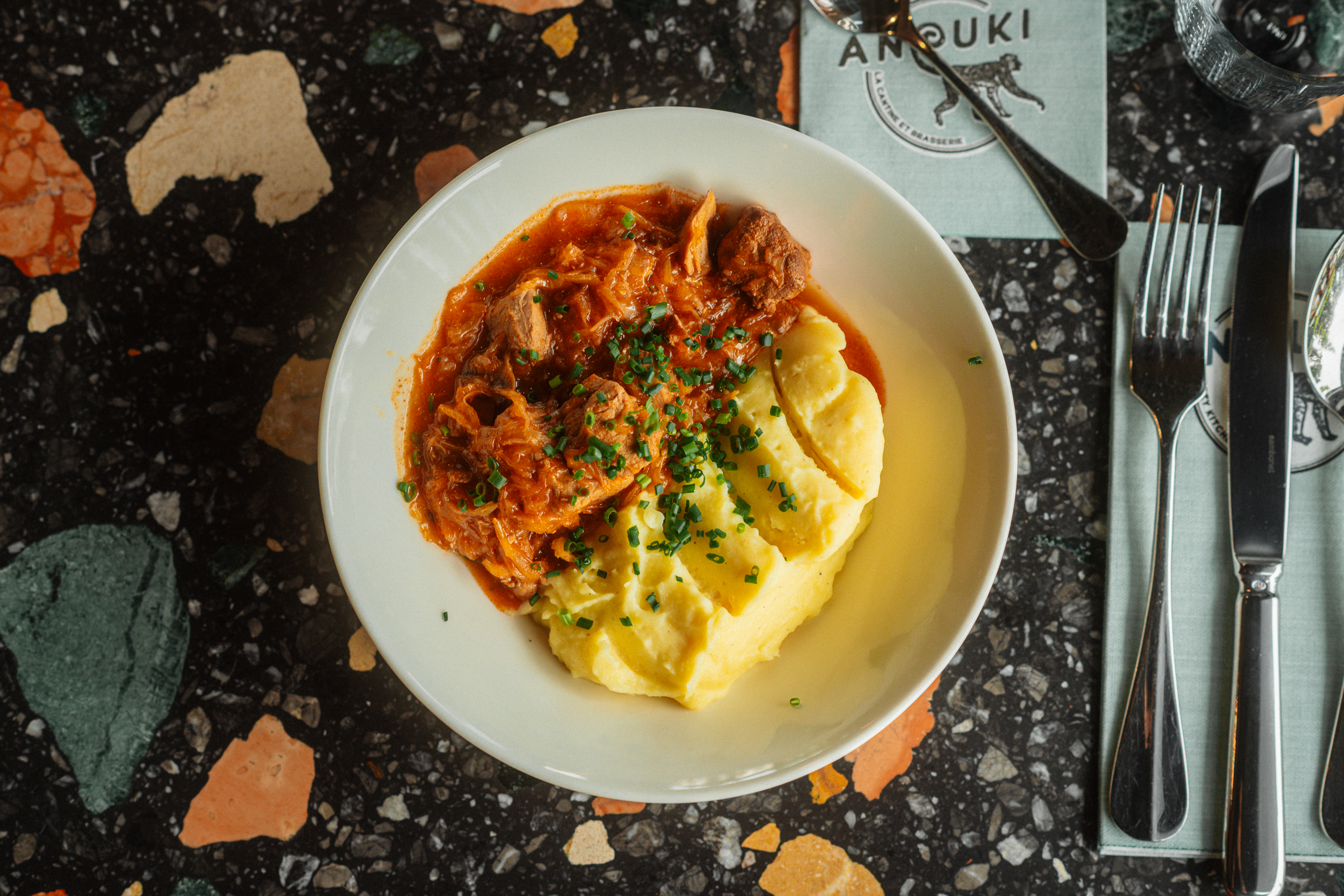 Anouki Kantine Osnabrück, Mittagsmenü, Mittagessen, Lunch, Essen, moderne Küche, Kantine, tiefer Teller weiß, Hausmannskost, Kartoffelstampf, Gulasch, Tomatensoße, Kräuter, Schnittlauch