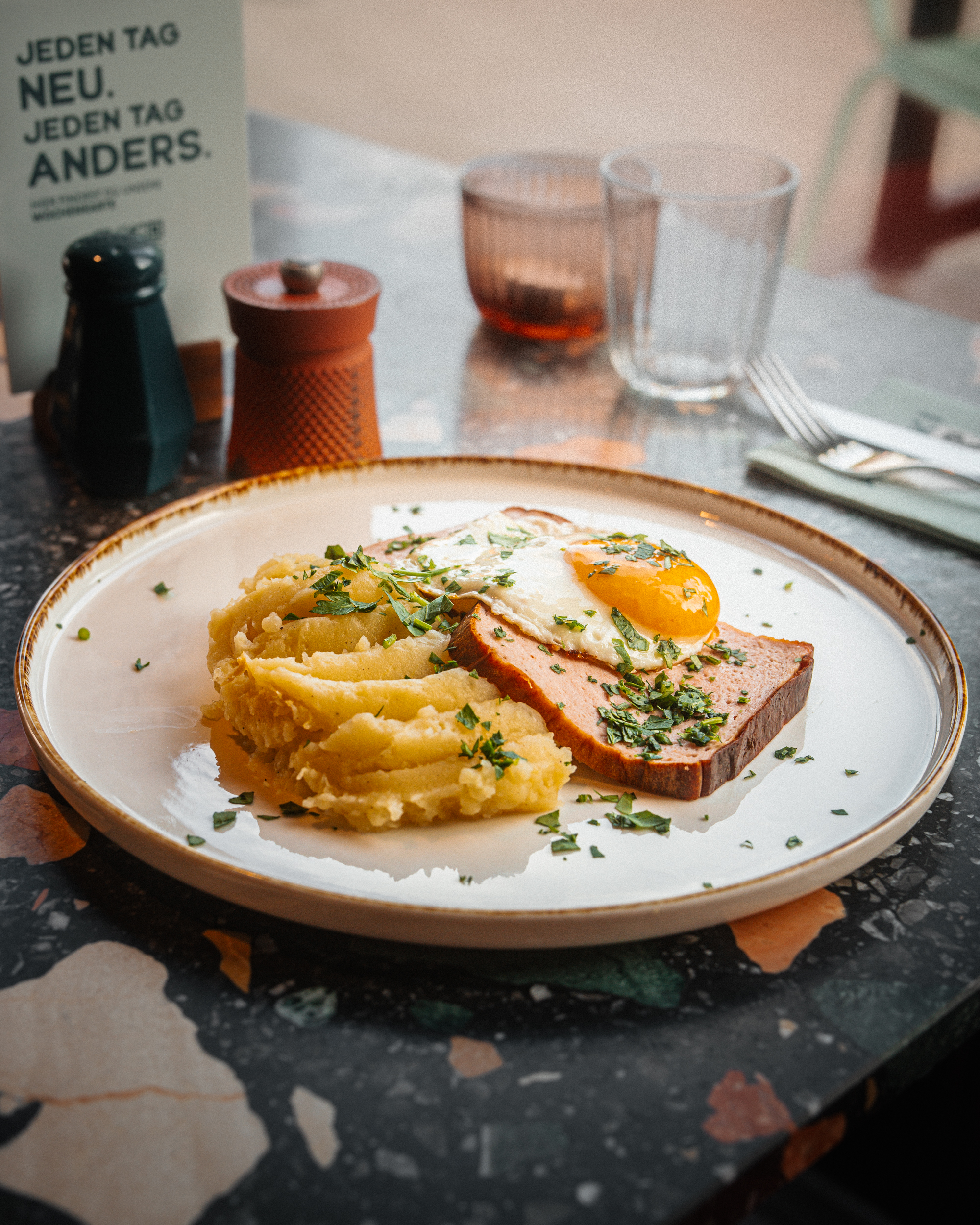Anouki Kantine Osnabrück, Mittagsmenü, Mittagessen, Lunch, Essen, moderne Küche, Kantine, Hausmannskost, flacher Teller beige, Kartoffelstampf, Spiegelei, Leberkäs, Kräuter, Petersilie